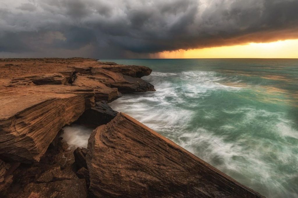 ساحل سنگی و صخره ای و دریای قشم پس از آسمان ابری و بارانی در زمان طلوع خورشید