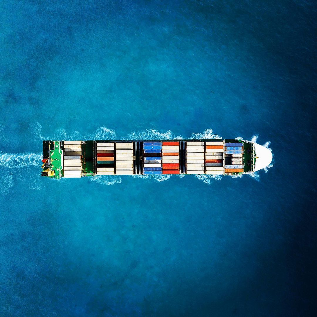 عکس هوایی با پهپاد از کشتی کانتینربر در حال حرکت در دریای زلال و پاک